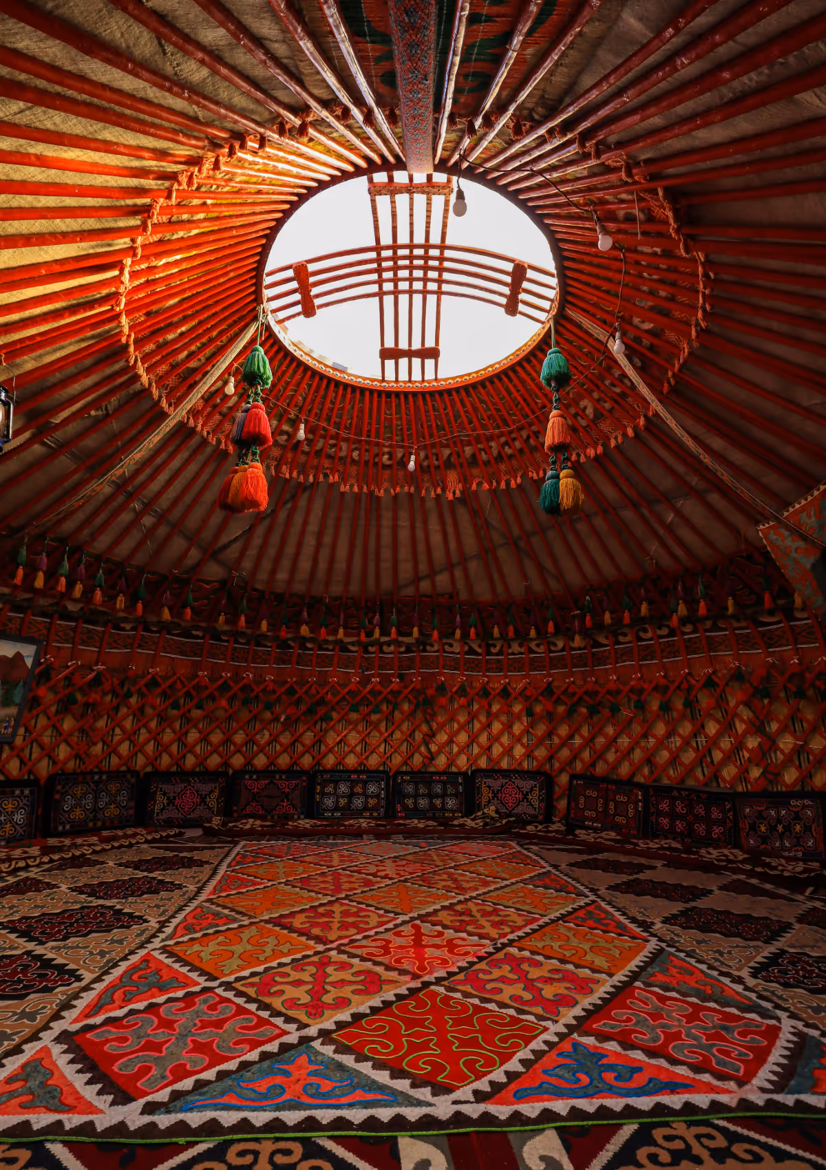 Intérieur d'une yourte traditionnelle avec un tapis coloré sur le sol et des éléments décoratifs suspendus sous le toit circulaire.