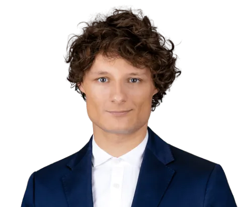 Porträt eines Mannes mit lockigem Haar, blauem Sakko und weißem Hemd vor transparentem Hintergrund.