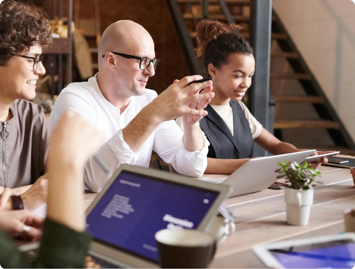 Menschen sitzen an einem Tisch und arbeiten zusammen mit Tablets und Laptops.