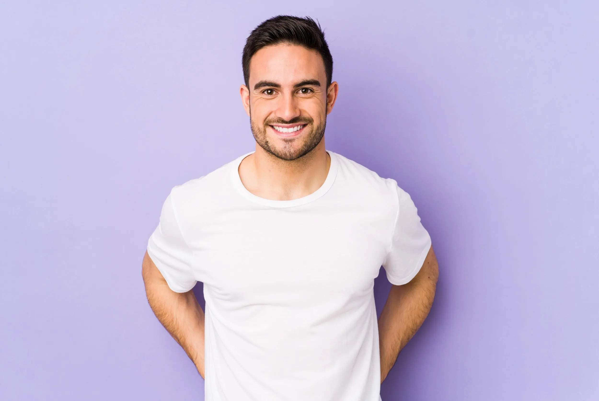A man standing against a purple wall with his hands on his hips