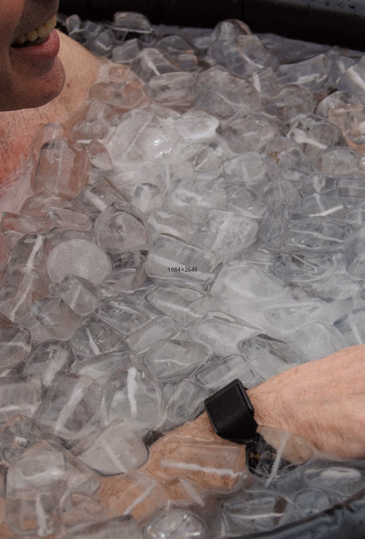 Hombre sonriendo sumergido en cubos de hielo hasta el cuello, con un reloj negro en la muñeca.