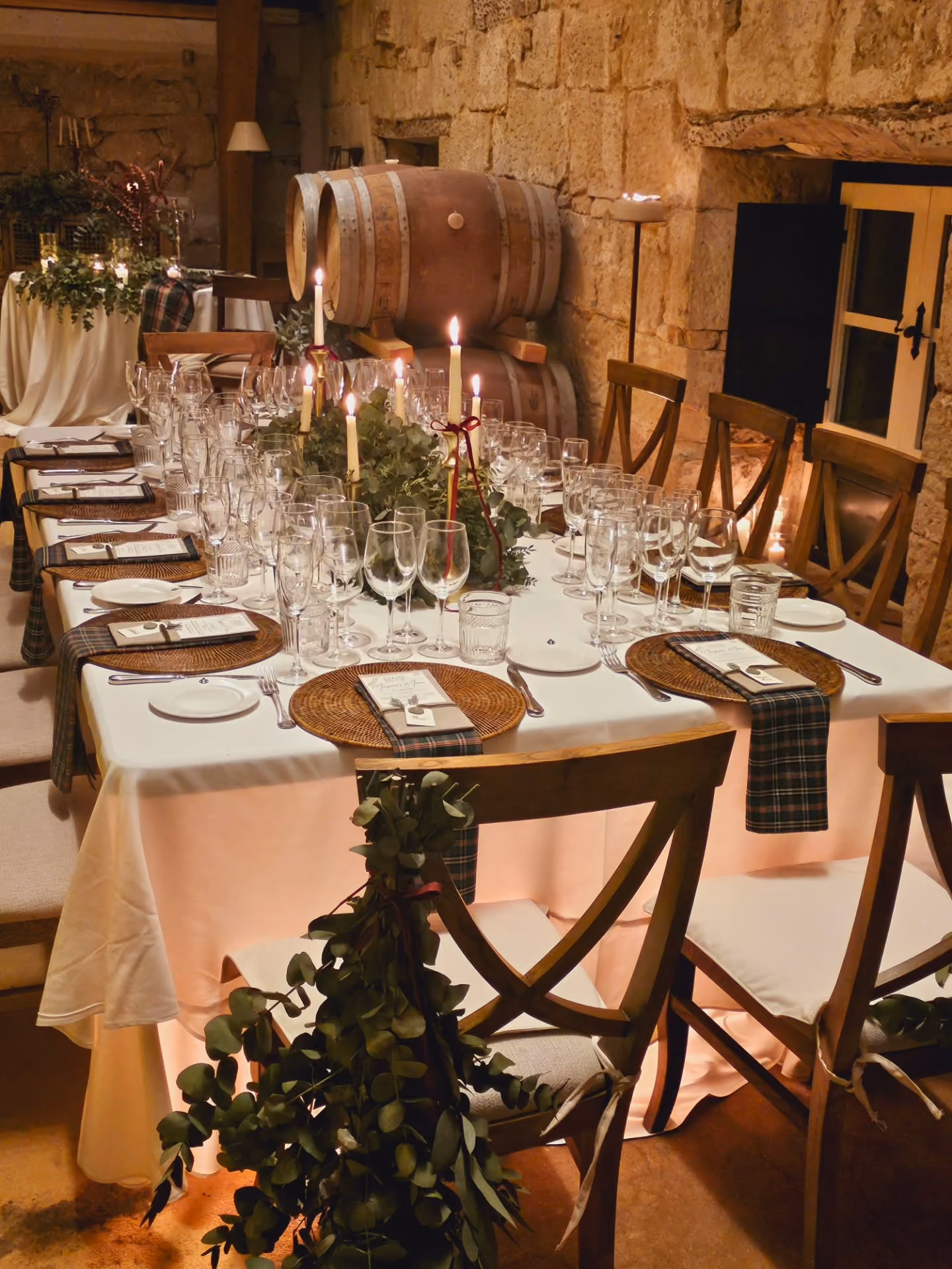 Mesa elegante con decoración de velas y folletos, ambiente cálido con barriles y paredes de piedra.