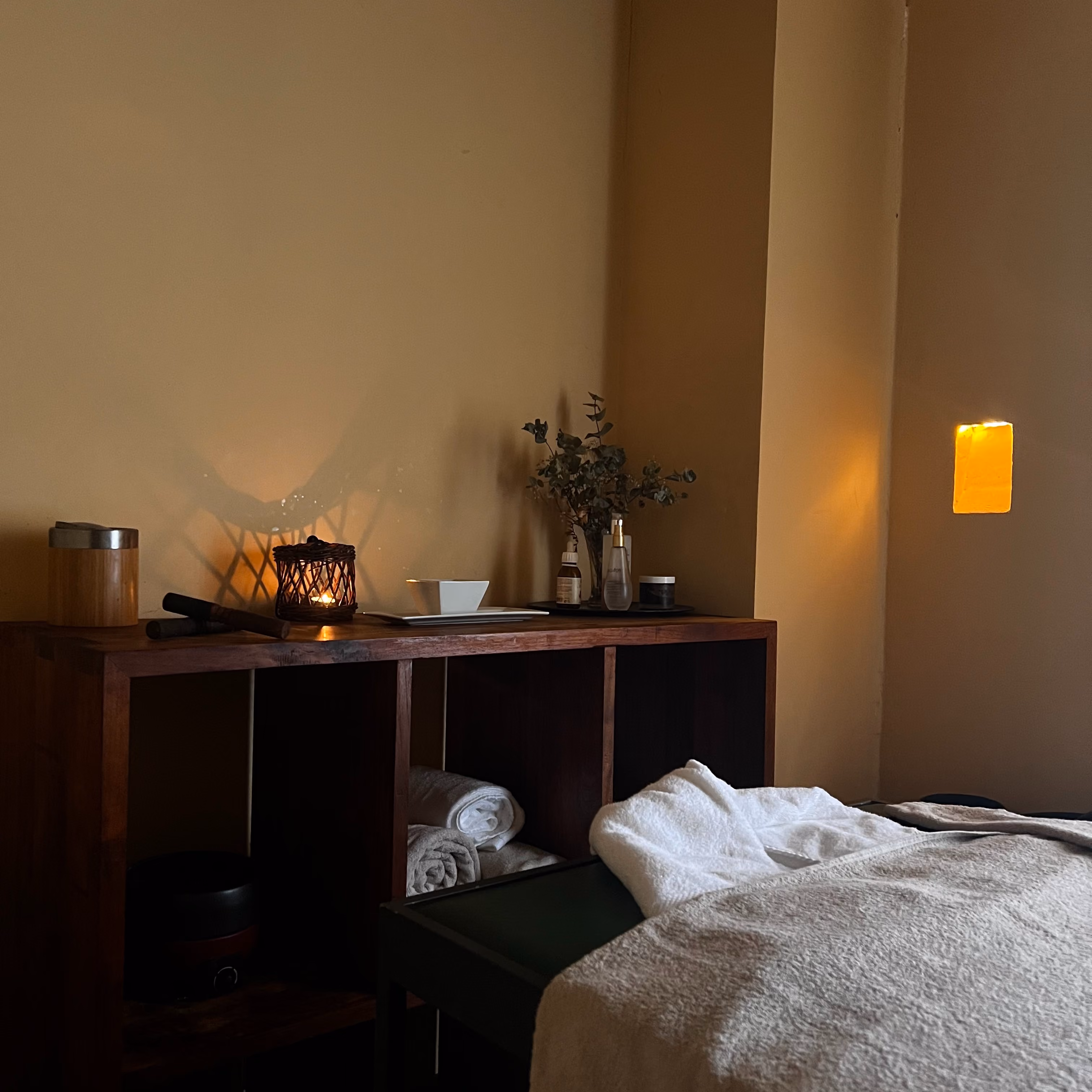 Habitación de spa con toallas, vela encendida y mesa de masajes cubierta con manta beige.