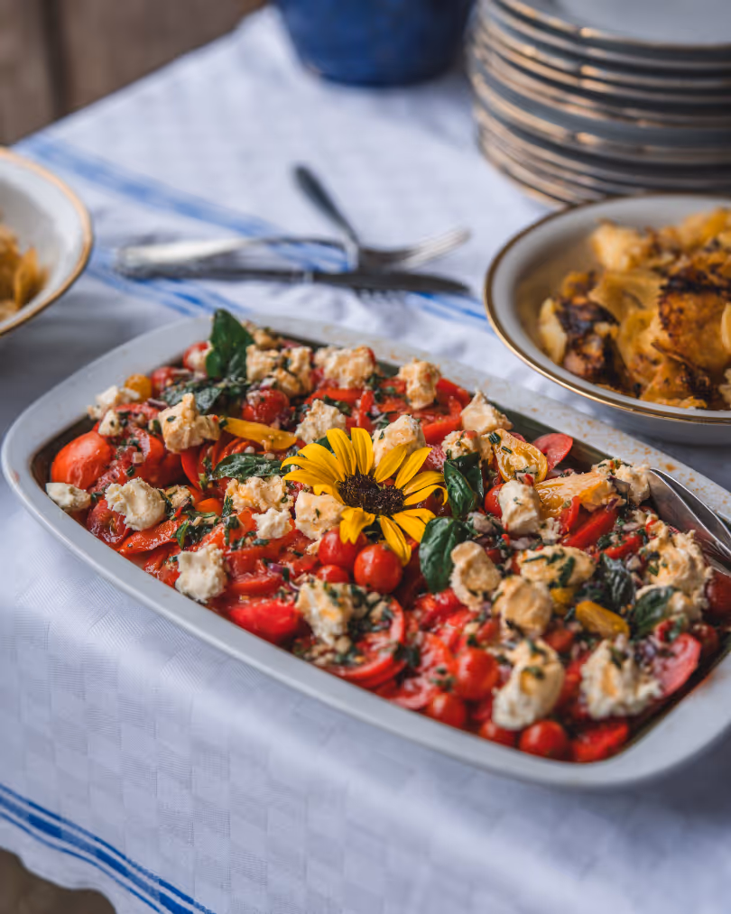 Baked dish with tomatoes, spinach, cheese, and herbs garnished with a yellow sunflower on a white and blue tablecloth.