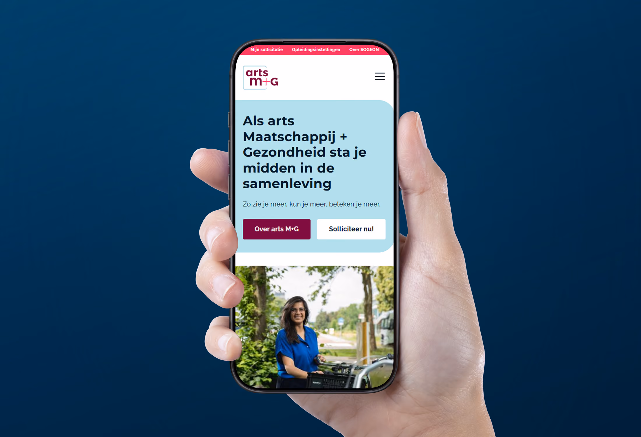 Hand houdt een smartphone met op het scherm de website van arts M+G, met tekst die zegt dat je als arts maatschappij en gezondheid midden in de samenleving staat, en een foto van een vrouw met een fiets in een buitenomgeving.
