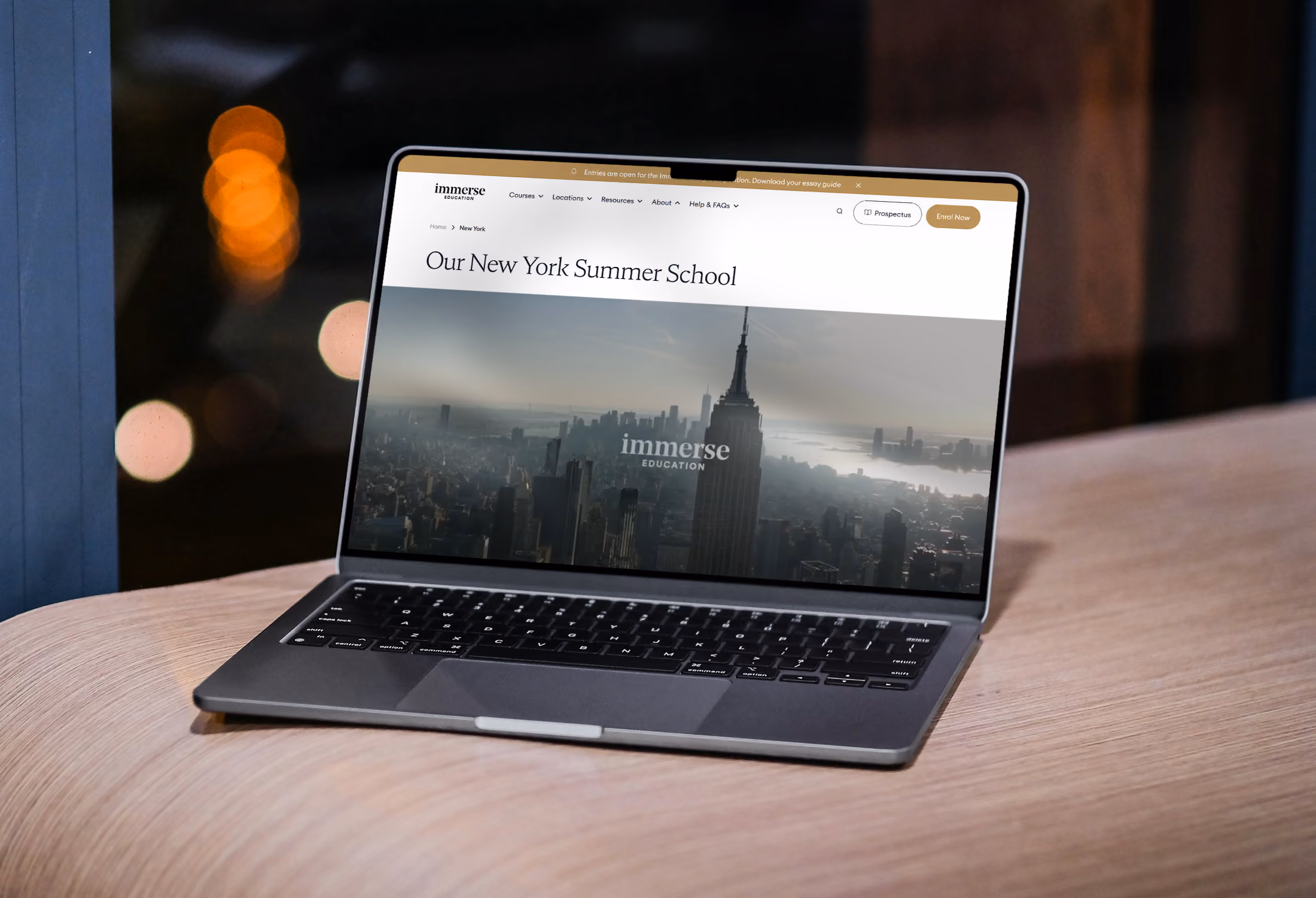 Laptop op een houten tafel met een website over de New York Summer School van Immerse Education, met een afbeelding van de skyline van New York en het Empire State Building.