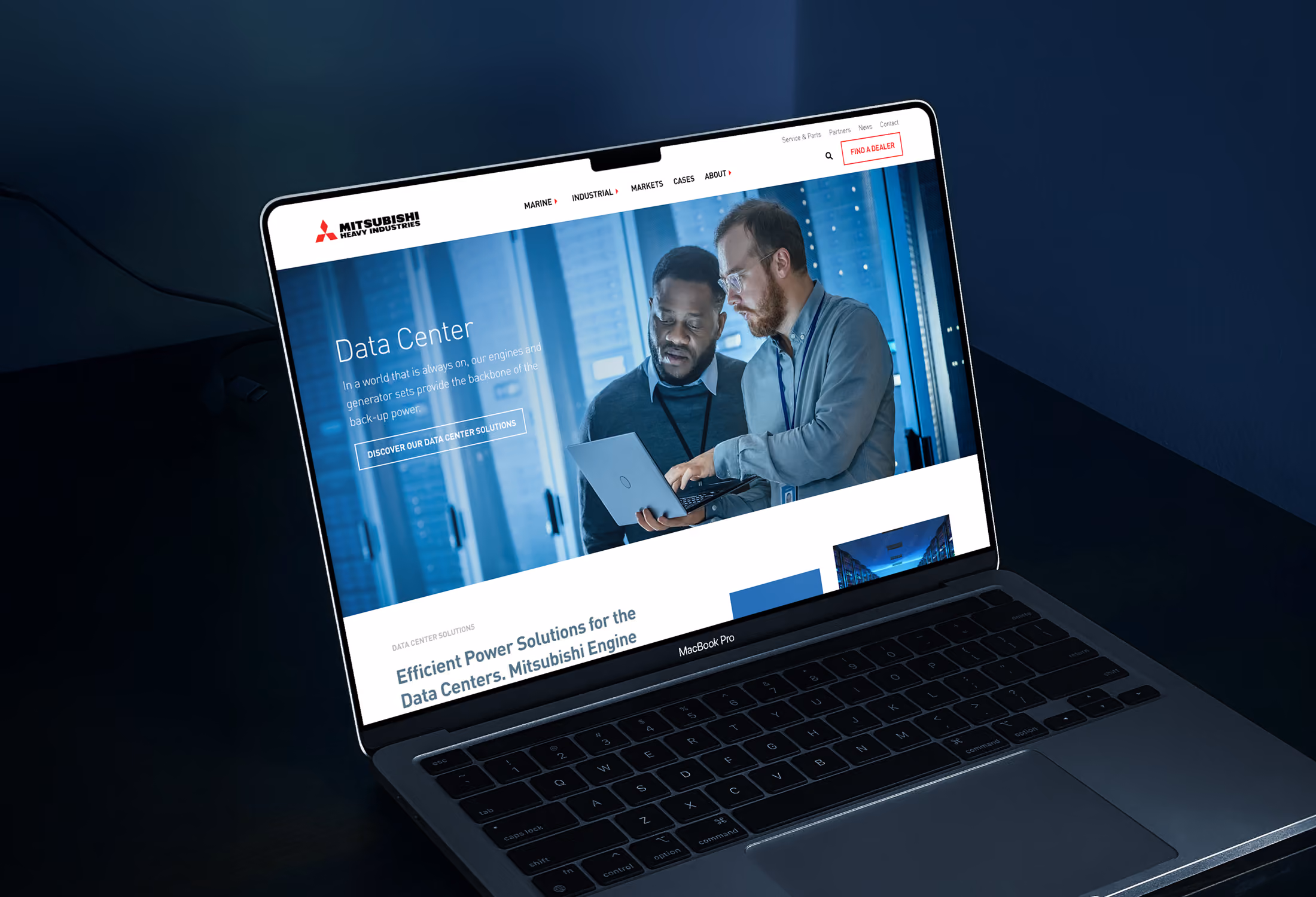 Een laptop waarop een webpagina van Mitsubishi Heavy Industries wordt weergegeven, met twee mannen die samen naar een laptop kijken in een datacenteromgeving.