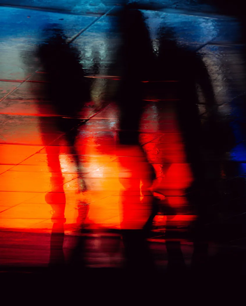 Young woman wearing a knitted hat with a pom-pom and a blue jacket, outdoors near rocky terrain at dusk.