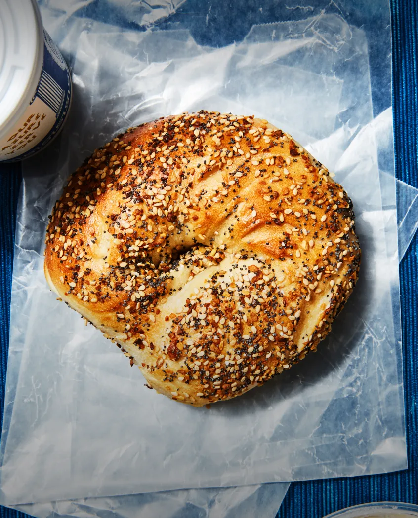 Young woman wearing a knitted hat with a pom-pom and a blue jacket, outdoors near rocky terrain at dusk.