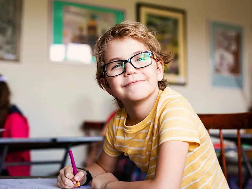 Lachende jongen met bril aan een schooltafel, Qurius