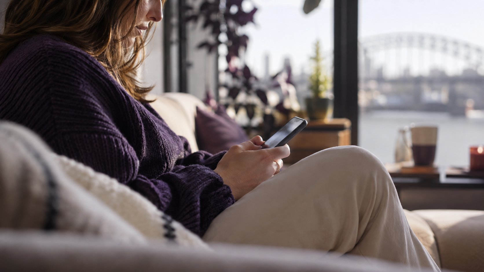 Vrouw zoekt iets op haar telefoon op de bank bij het raam