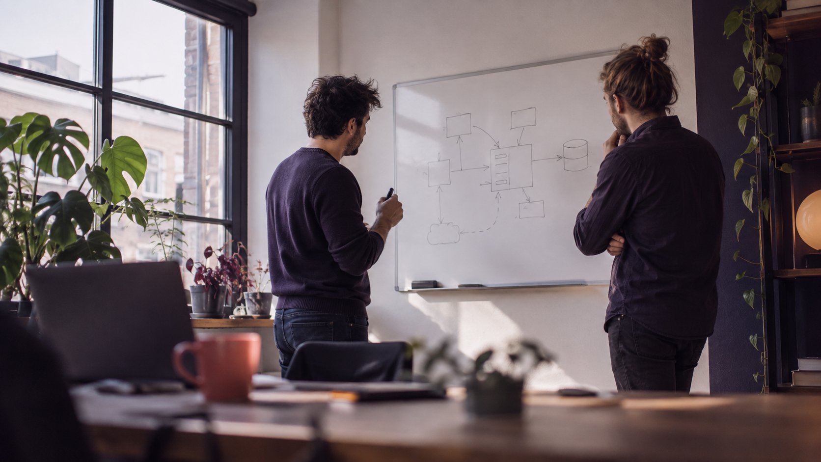 Twee ontwikkelaars bekijken een schets van een systeemarchitectuur op een whiteboard