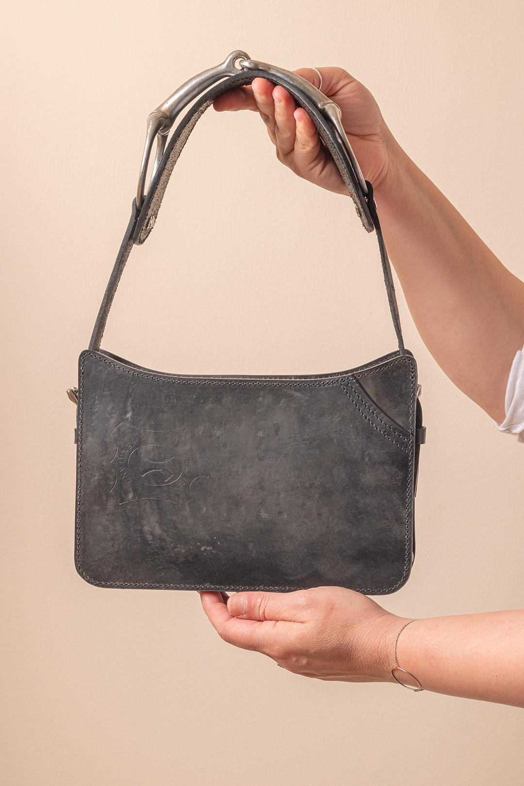 Hands holding a black leather handbag with a short strap against a beige background.