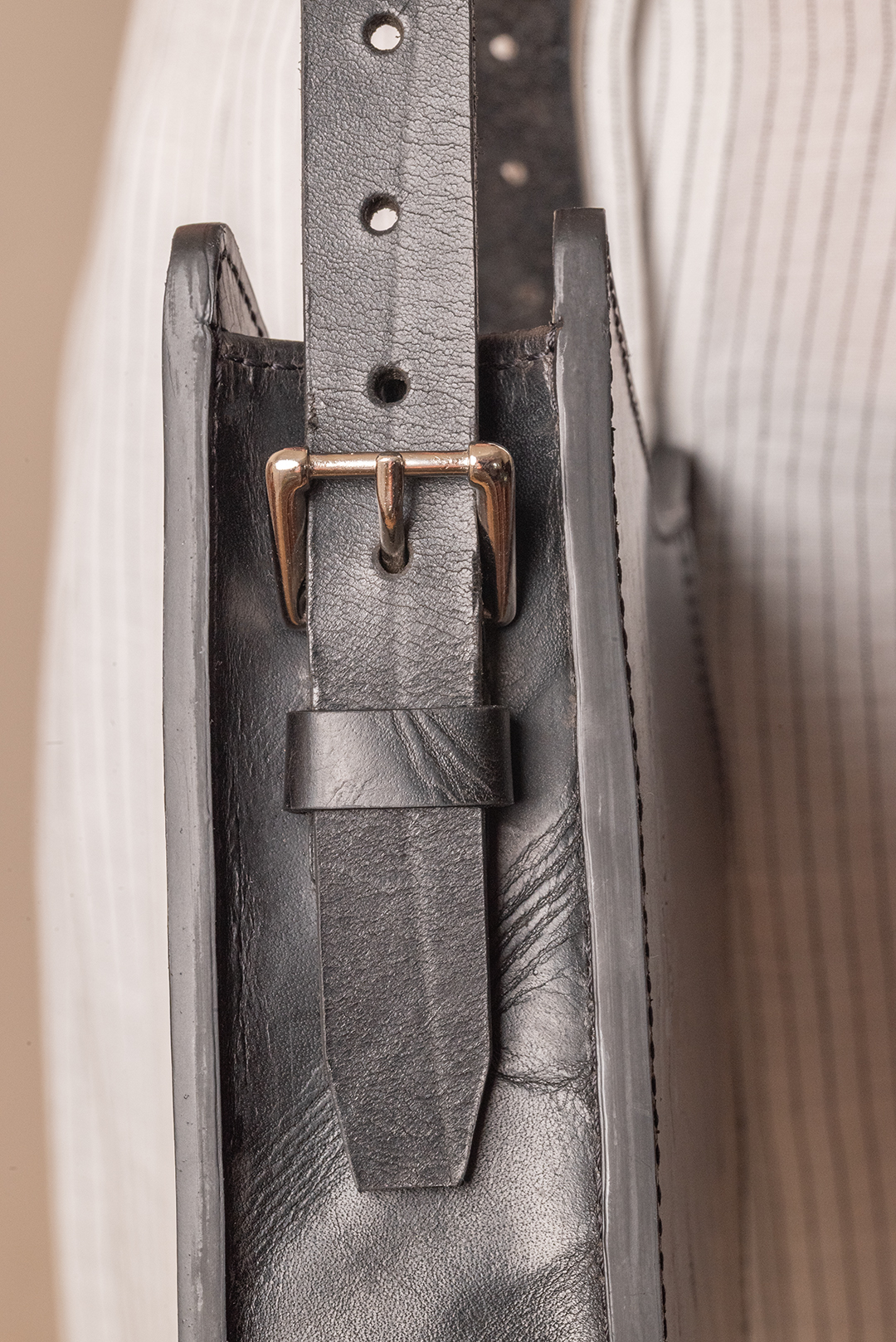 Close-up of a black leather belt with a silver buckle threaded through a leather loop.