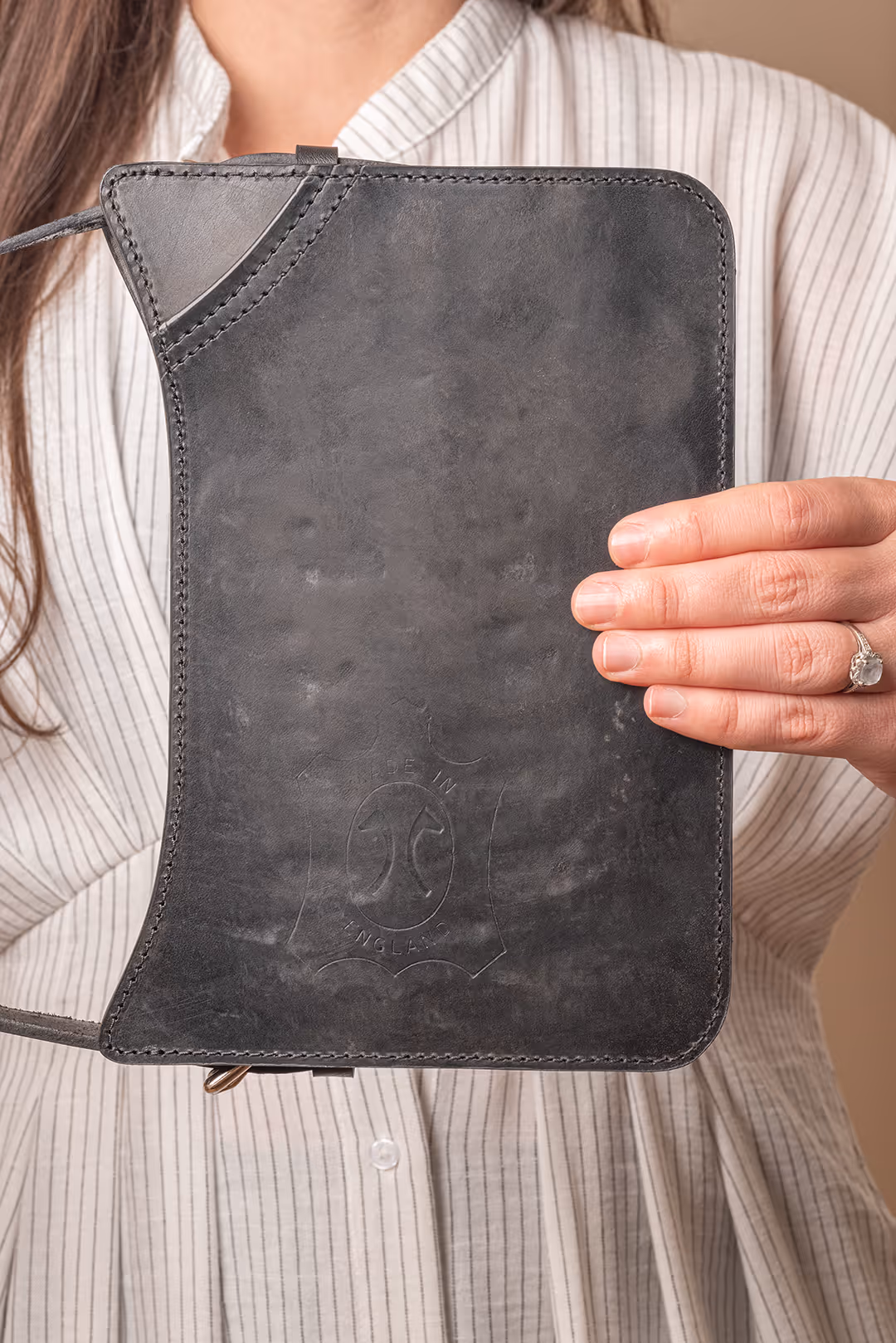Close-up of a woman holding a dark grey leather pouch embossed with a 'Made in England' mark.