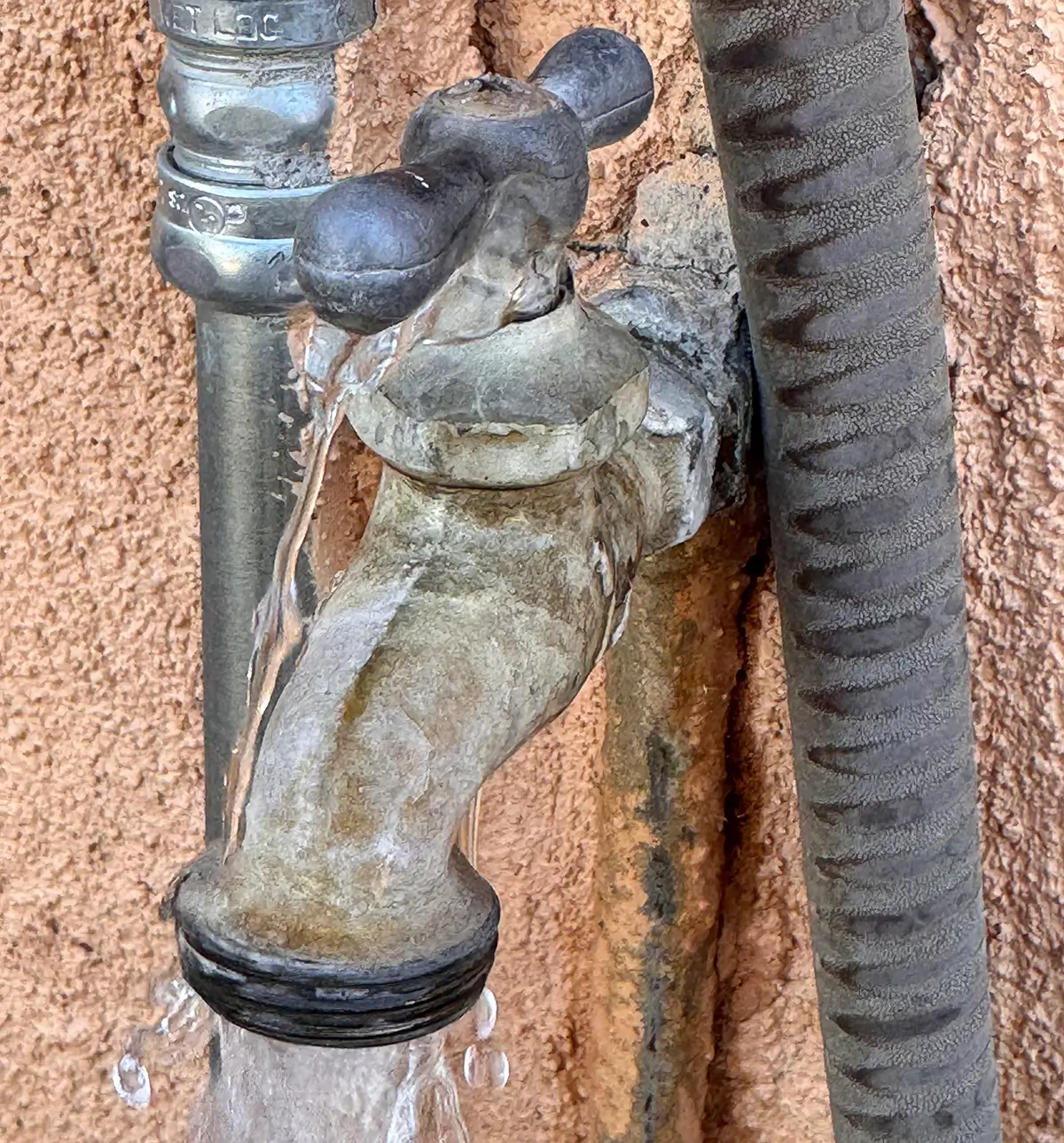 Example of common household leaks — an outdoor faucet dripping water from the handle and spout against a stucco wall