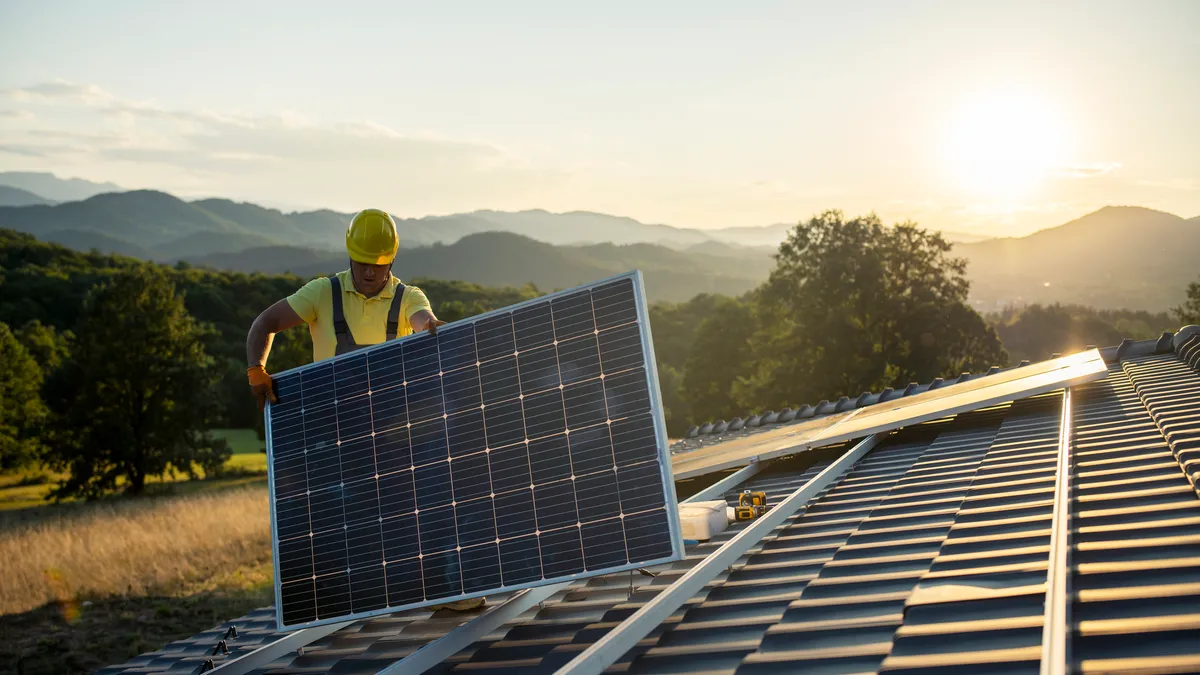 Solar worker installing solar panel on roof of house with mountains in background and sun setting
