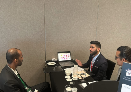 Three men in business attire having a discussion around a table with a laptop and water glasses.