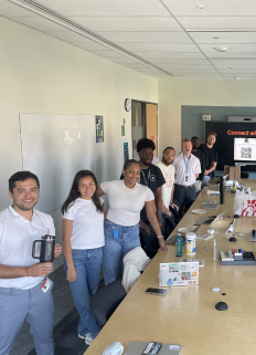 Seven people standing in a line along a conference table in a modern office, smiling at the camera.
