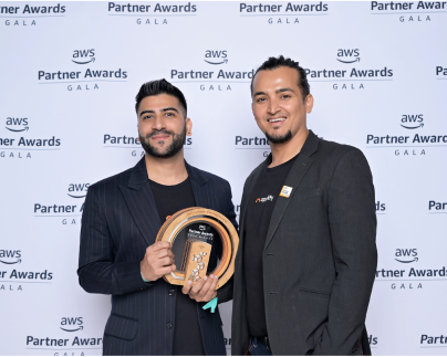 Two men smiling and posing with an AWS Partner Awards trophy in front of a step-and-repeat banner at the AWS Partner Awards Gala.