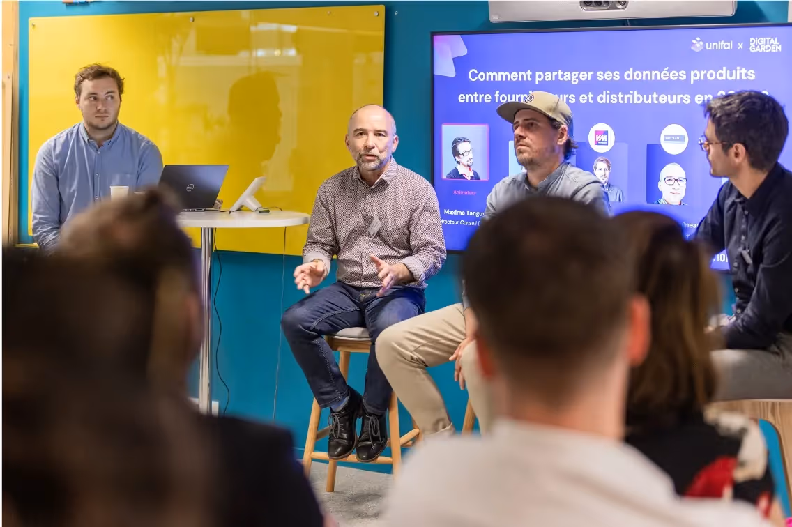 Quatre hommes discutent lors d'un panel tech avec public vu de dos en avant-plan.