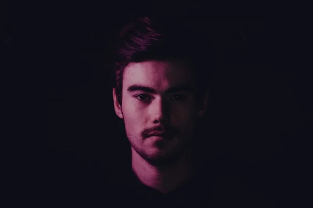 Portrait of a man against a dark background with purple lighting. Photo by lucas clarysse on Unsplash