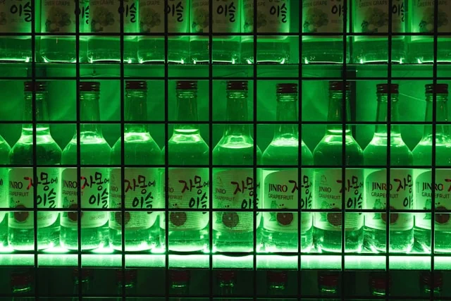 Rows of green soju bottles displayed behind a metal grid. Photo by Valentin on Unsplash