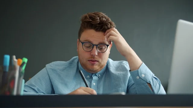 A man working at a computer with his hand against his forehead.