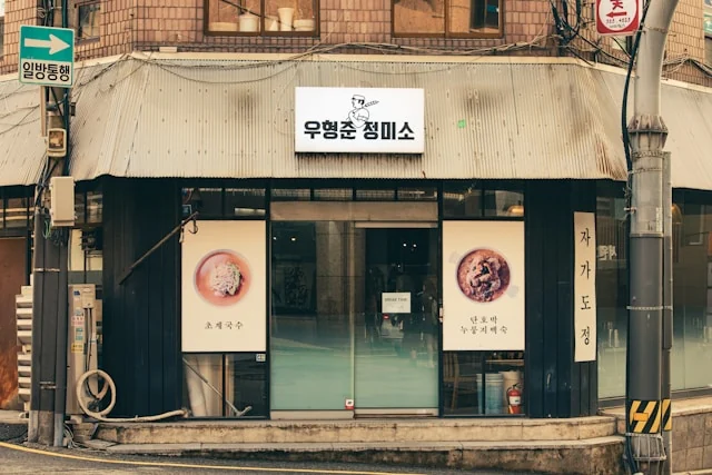 A Korean restaurant entrance with a fabric awning and menu displays. Photo by HorseRat on Unsplash