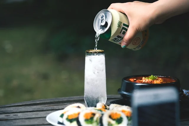 A drink being poured beside gimbap and a bowl of food. Photo by Ryan Kwok on Unsplash