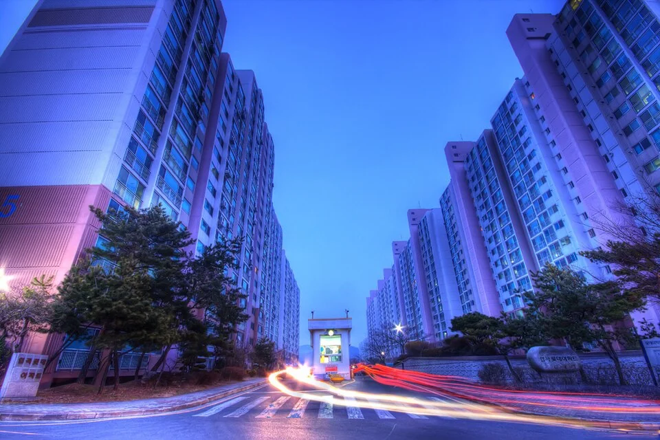 Apartment towers at dusk with vehicle light trails in the foreground. Image Credit: Wikimedia