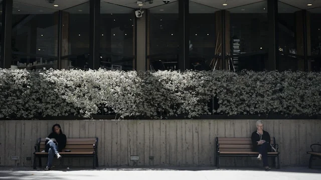 Two people sitting separately on outdoor benches.