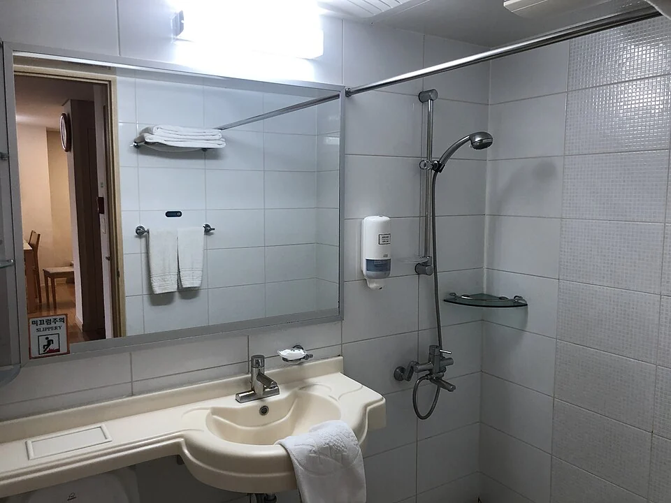 A tiled bathroom with a sink, mirror and handheld shower.