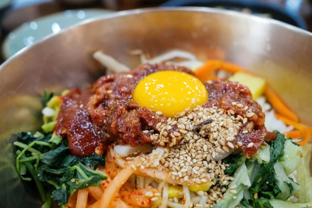 Bibimbap topped with vegetables, sliced beef, sesame seeds and an egg yolk.