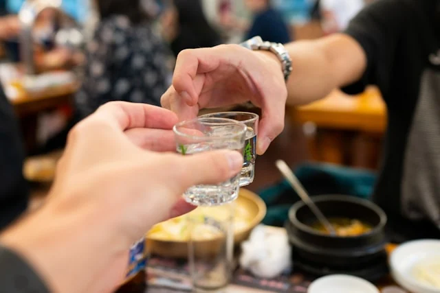 People clinking small glasses across a restaurant table.