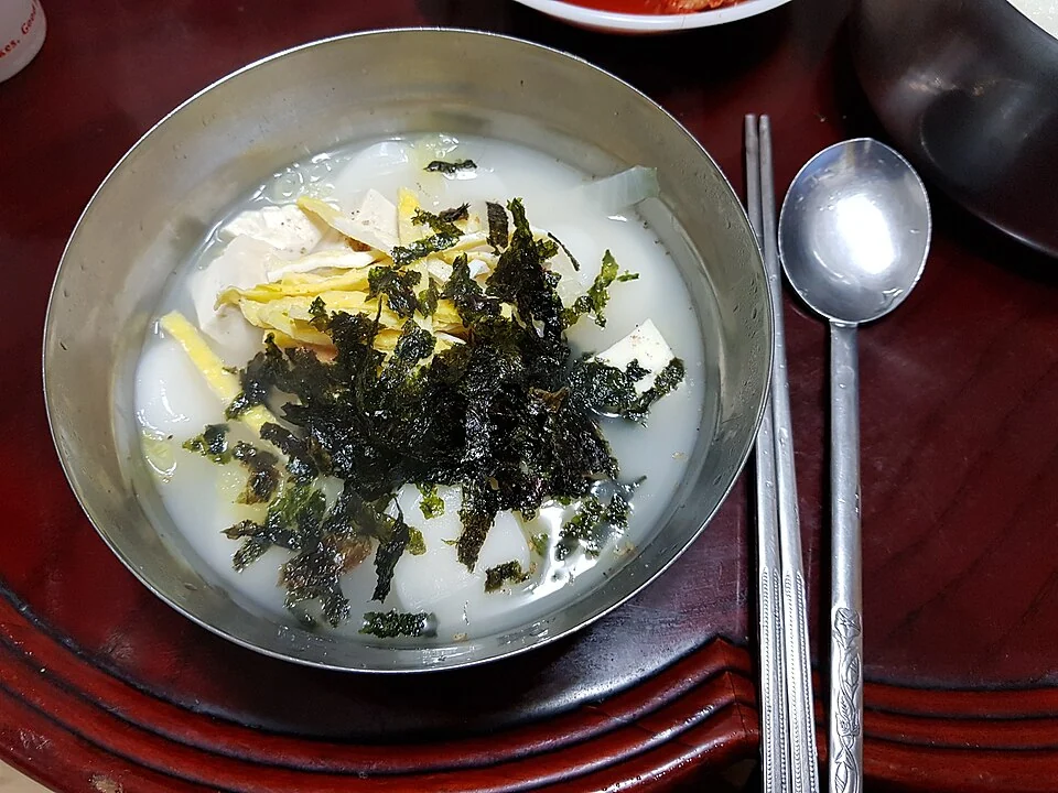 Tteokguk rice cake soup garnished with egg and shredded seaweed.