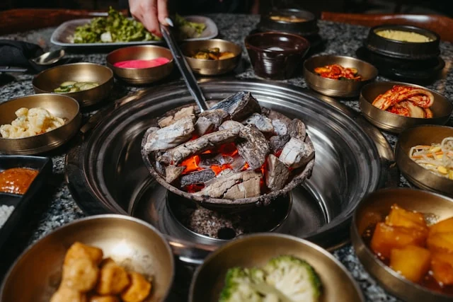 Meat cooking on a Korean barbecue grill surrounded by side dishes.