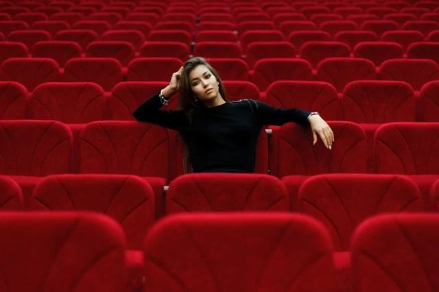 A person sitting among rows of red cinema seats.