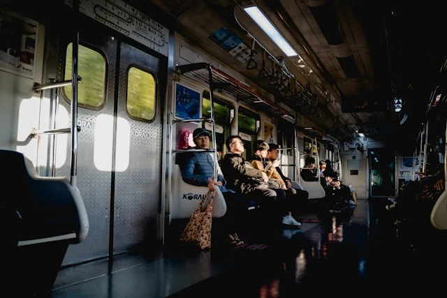 Passengers sitting quietly inside a sunlit subway carriage.