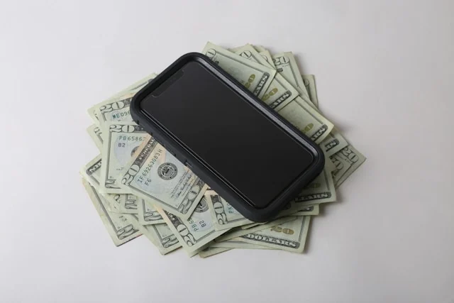 A smartphone resting on a spread of US dollar banknotes. Photo by Giorgio Trovato on Unsplash