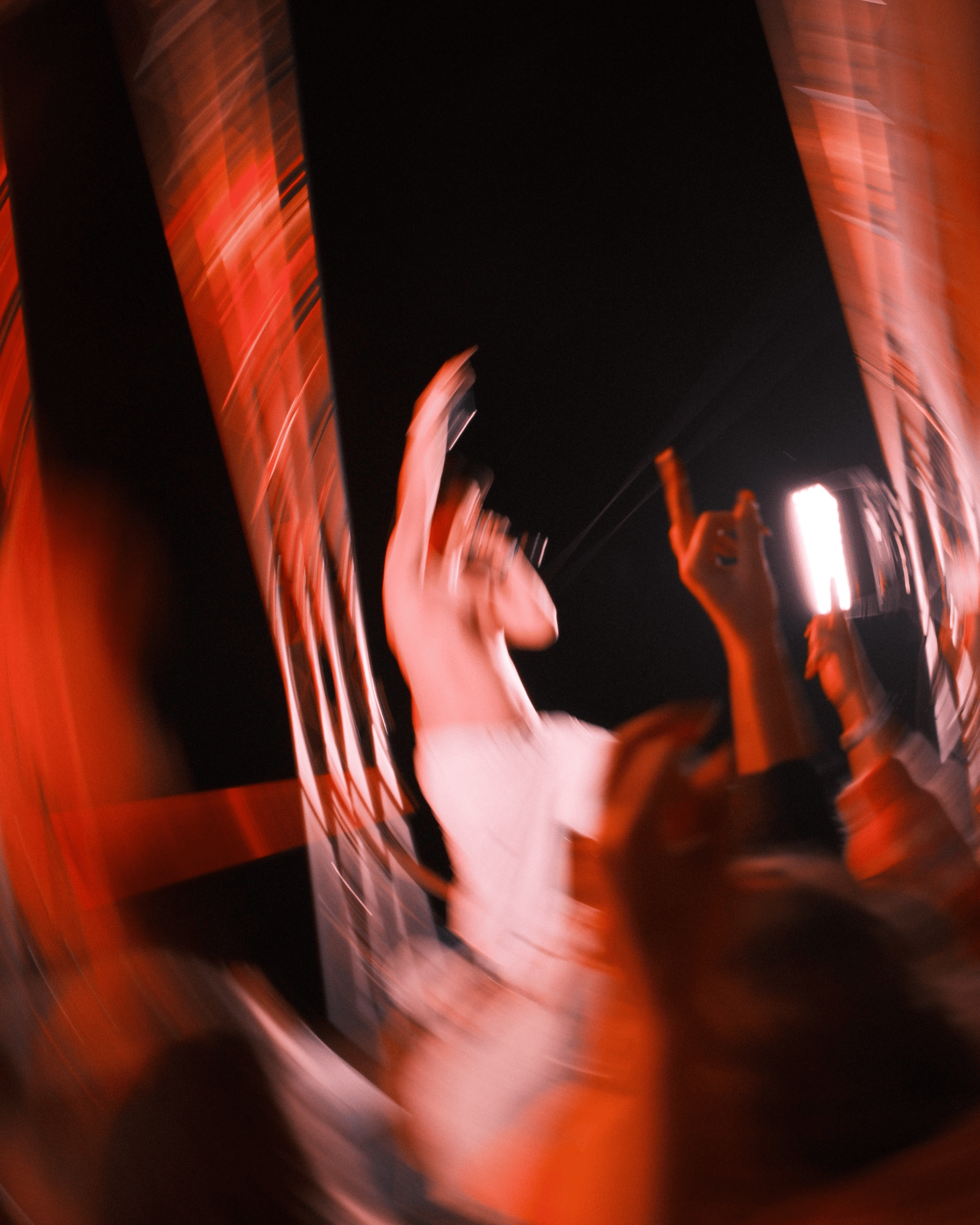 Et uskarpt, virvlende bilde av en artist på scenen med en mikrofon, omgitt av opprakte hender i publikum. Rødt og oransje lys skaper en dynamisk og energisk atmosfære.
