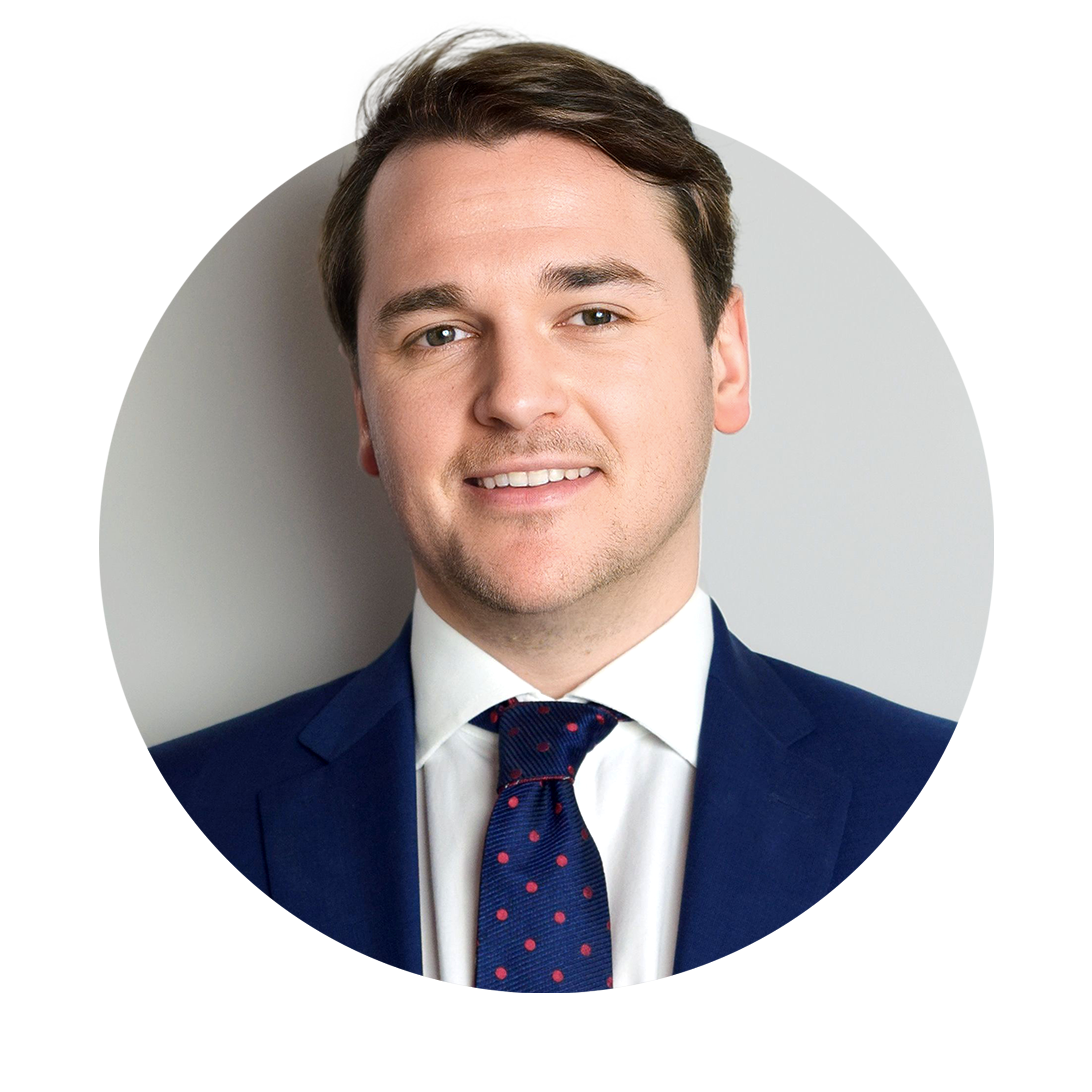 Smiling young man with brown hair wearing a blue suit, white shirt, and navy tie with red polka dots.