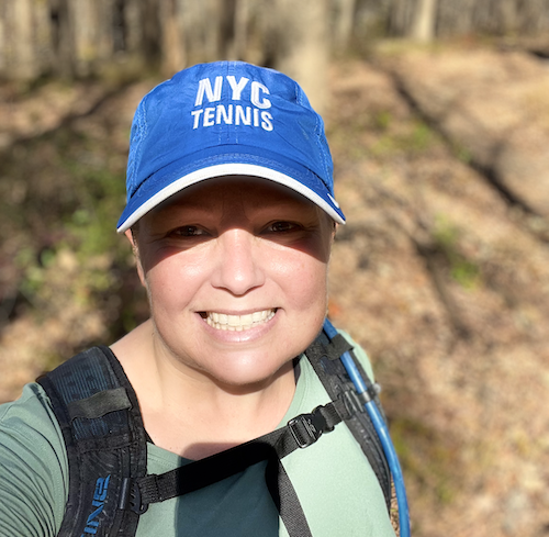 A photo of Laura Cochran smiling with a blue NYC tennis hat.
