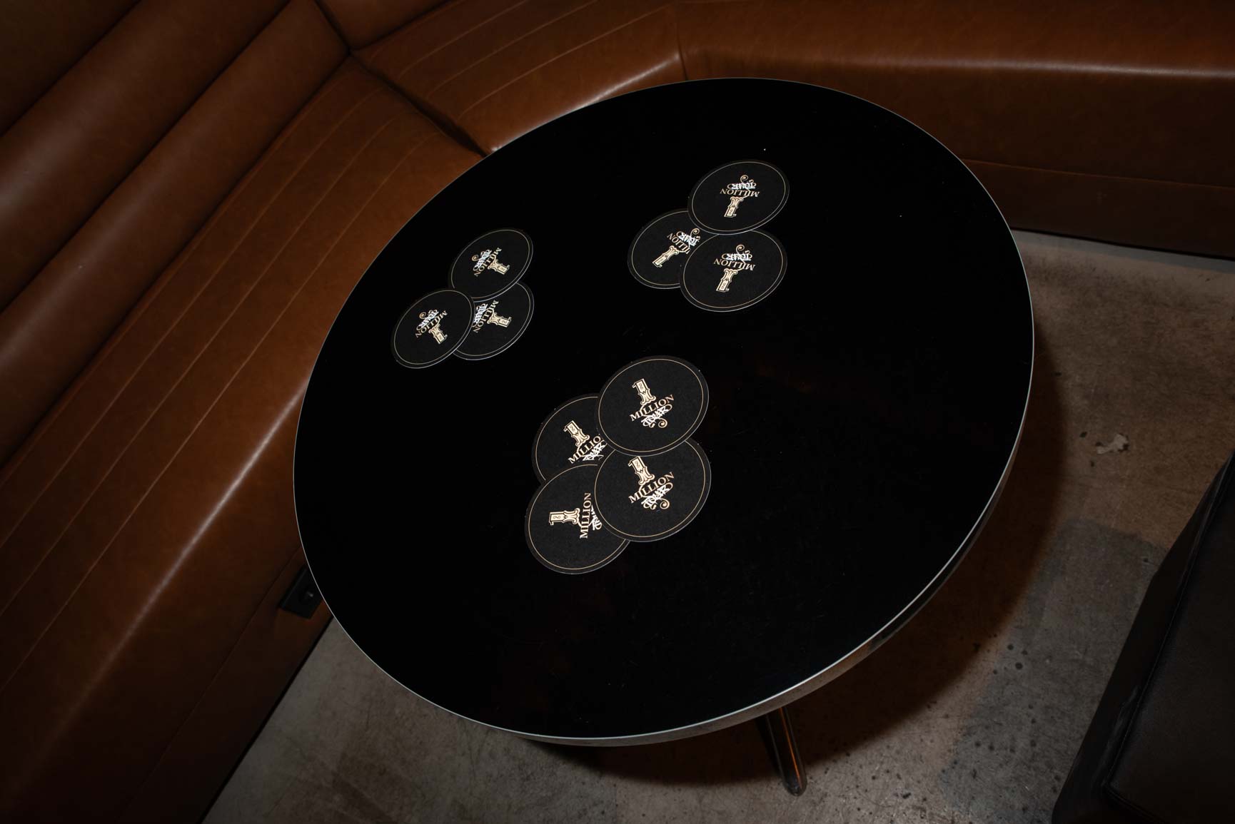 Round black table with Rabanne One Million branded coasters and brown leather banquette seating, branding detail from the pop-up in Madrid