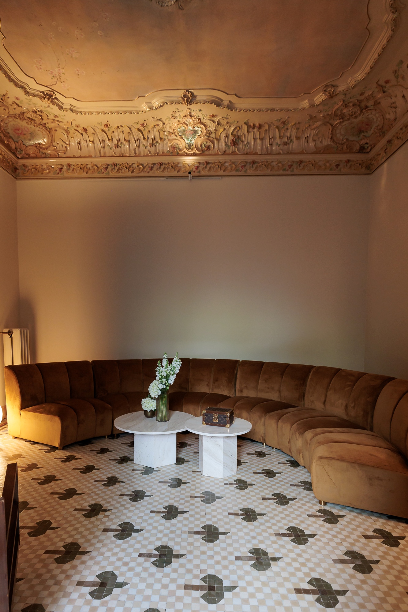 Semi-circular camel velvet sofa and white marble table on mosaic floor, interior of the Louis Vuitton Cruise 2025 Resee event