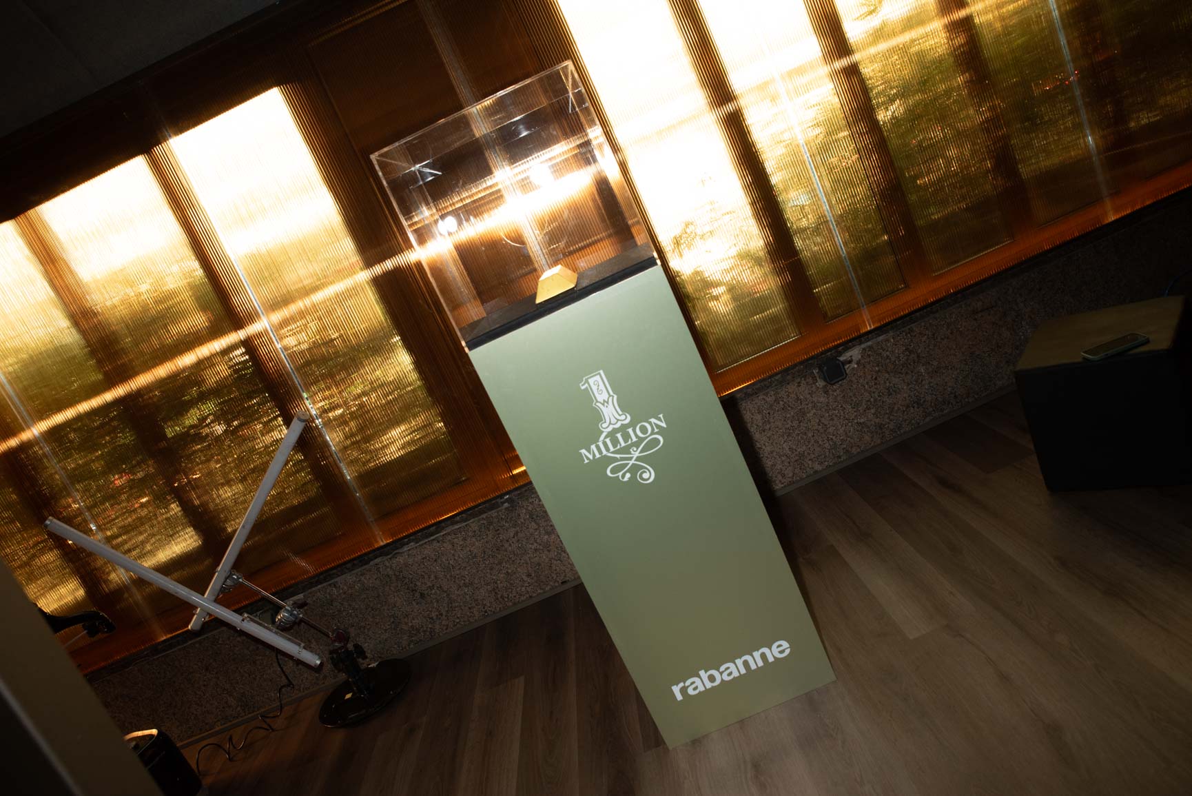 Pedestal de exposición con vitrina de cristal y logo de Rabanne One Million, vista cenital con pared dorada traslúcida