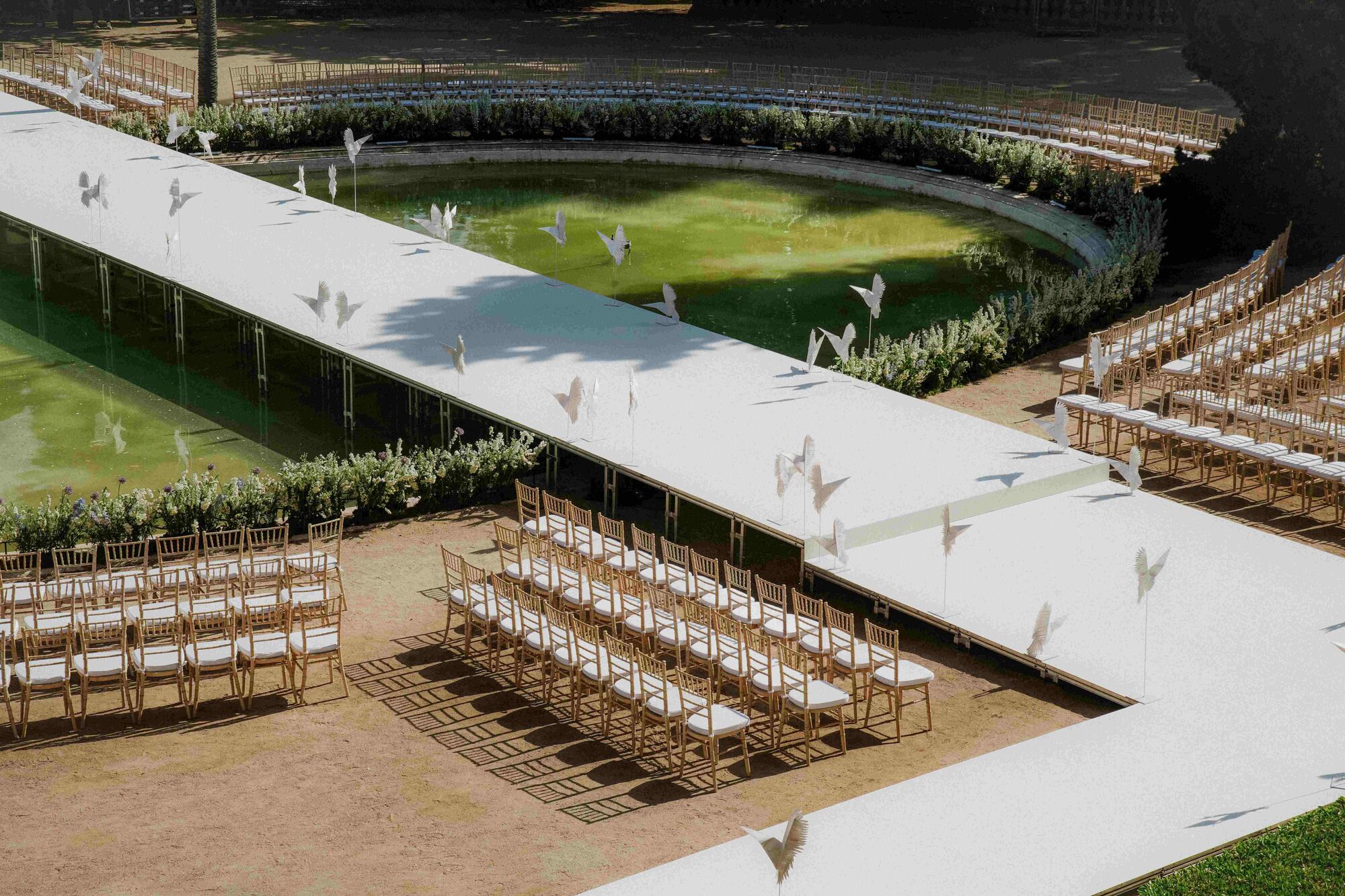 Pasarela blanca sobre el estanque del Palau Reial de Pedralbes con sillas para invitados y pájaros de papel, desfile nupcial de Woná Concept & Eva Lendel producido por ESMA Events