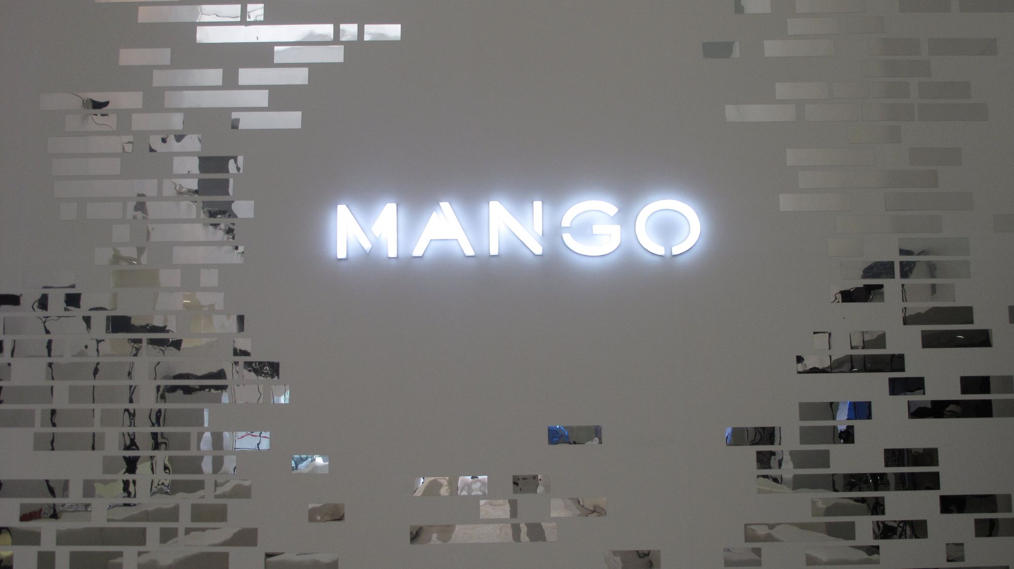Logotipo de Mango iluminado sobre una pared blanca con piezas de espejo, montaje de Mango Beijing SS 2012 producido por ESMA Events