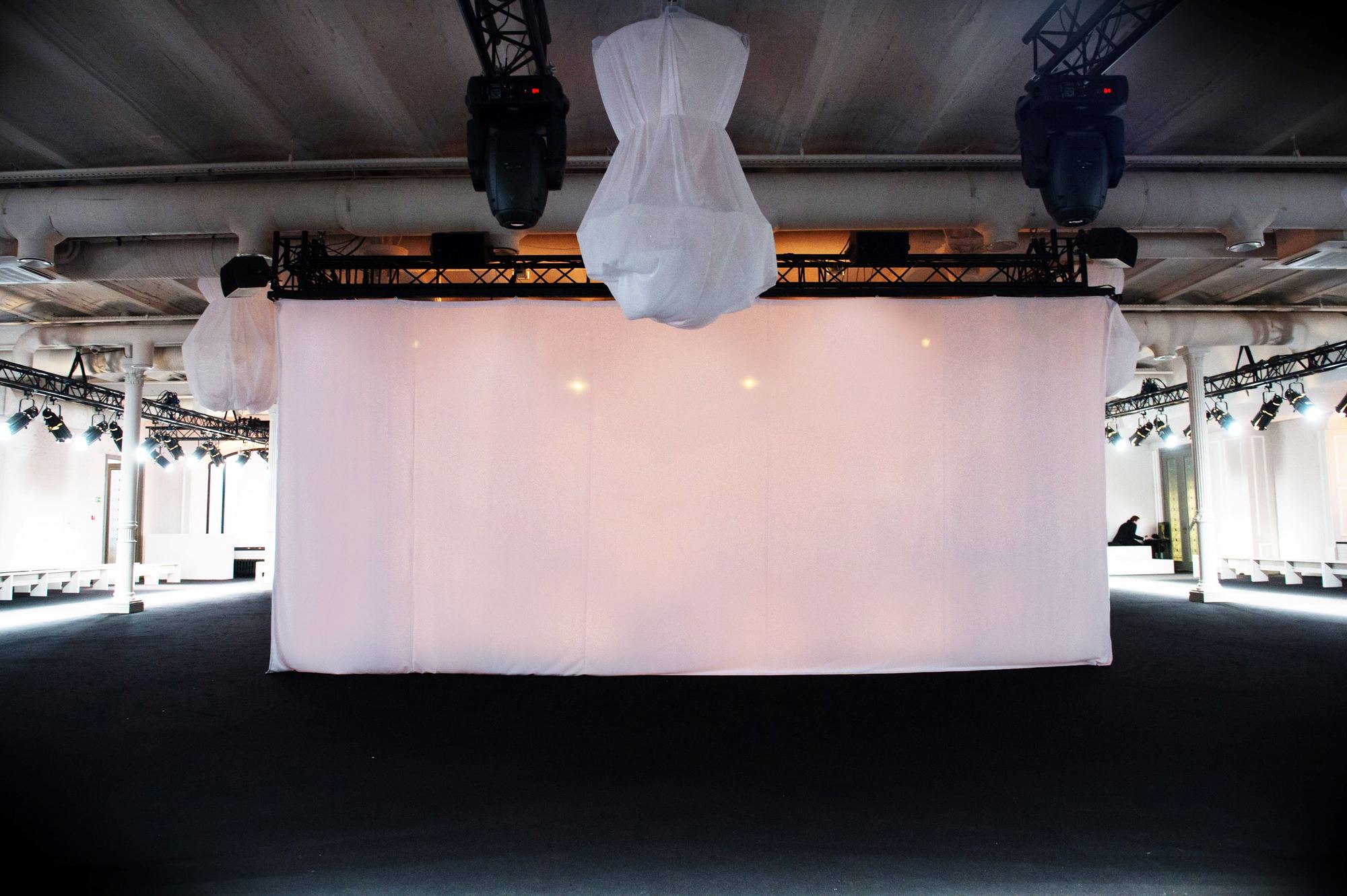 Pantalla de tela blanca suspendida bajo focos móviles en una sala diáfana con asientos en los laterales, montaje del Mango Fashion Show in Moscow producido por ESMA Events