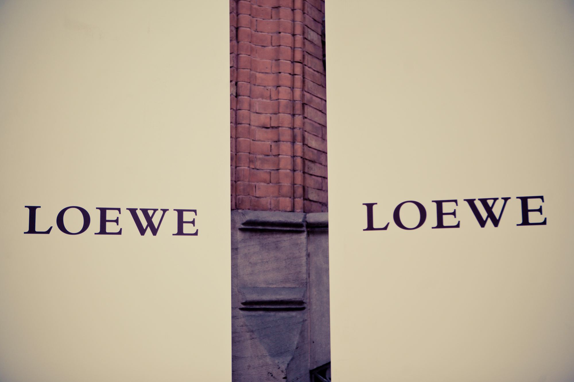 Logotipo de Loewe repetido a ambos lados de una columna de ladrillo sobre fondo crema, evento de Loewe producido por ESMA Events